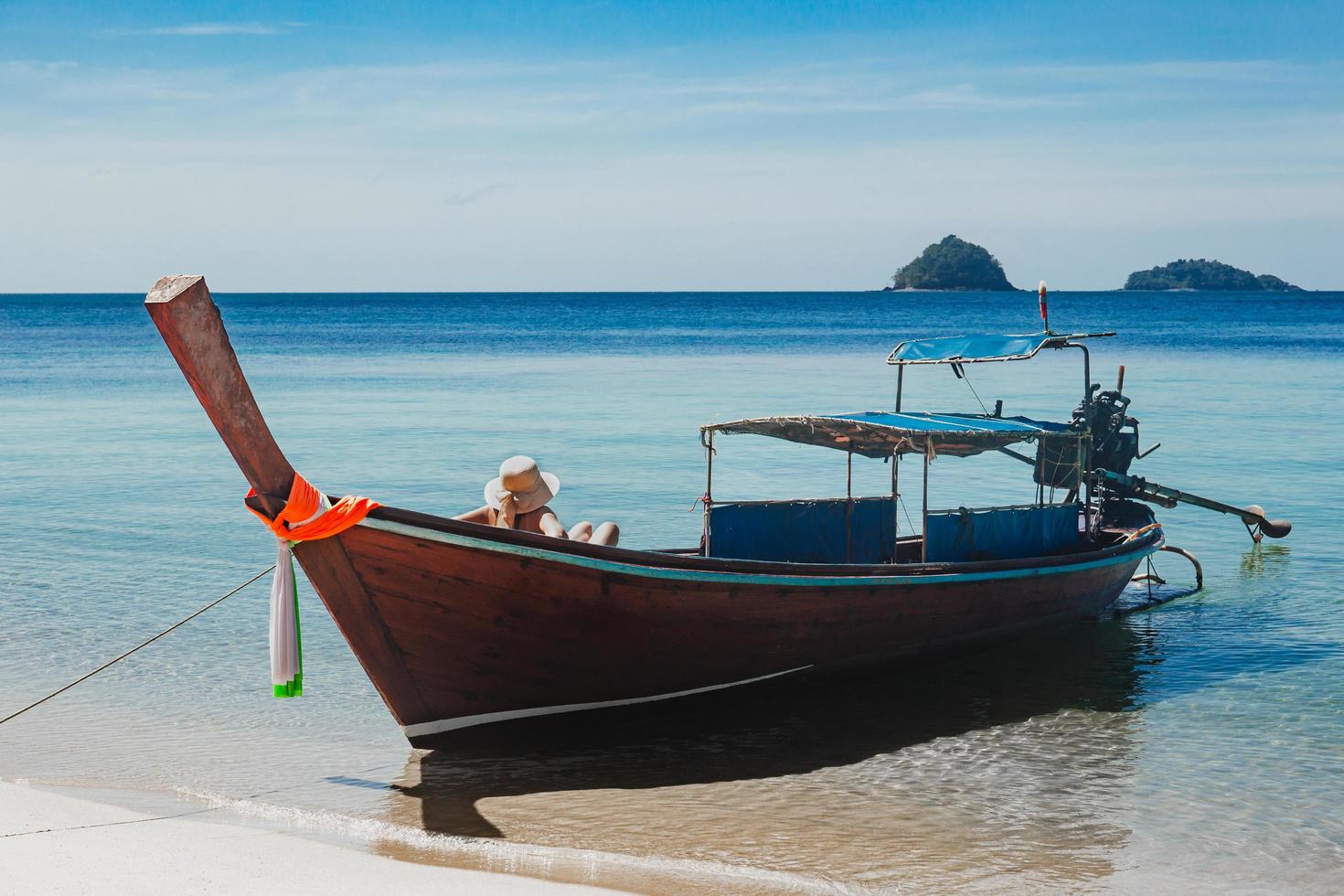 oidentifierad kvinna sitter på en träbåt i havet sola. foto