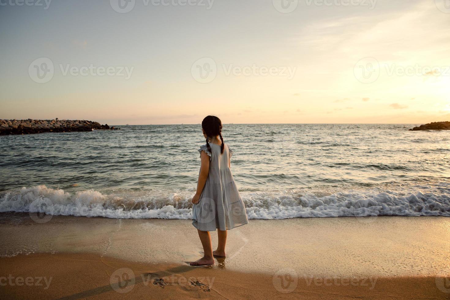 flicka barn står vid havet stranden mot vacker solnedgång ljus foto