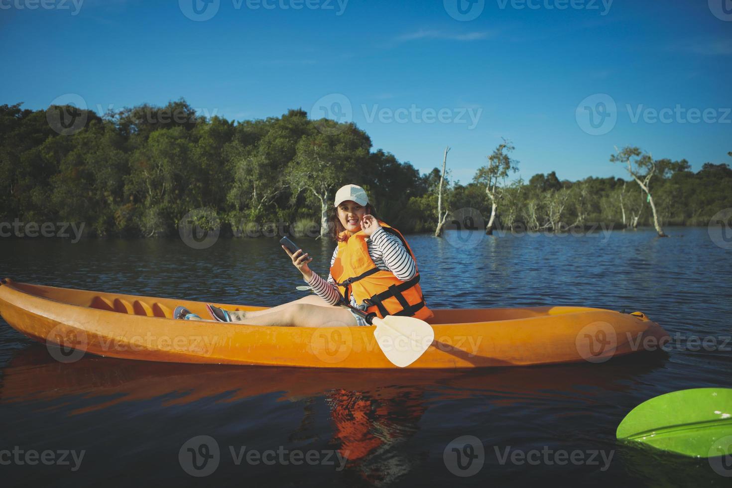 yngre kvinna sitter i havskajak och håller smartphone i handen foto