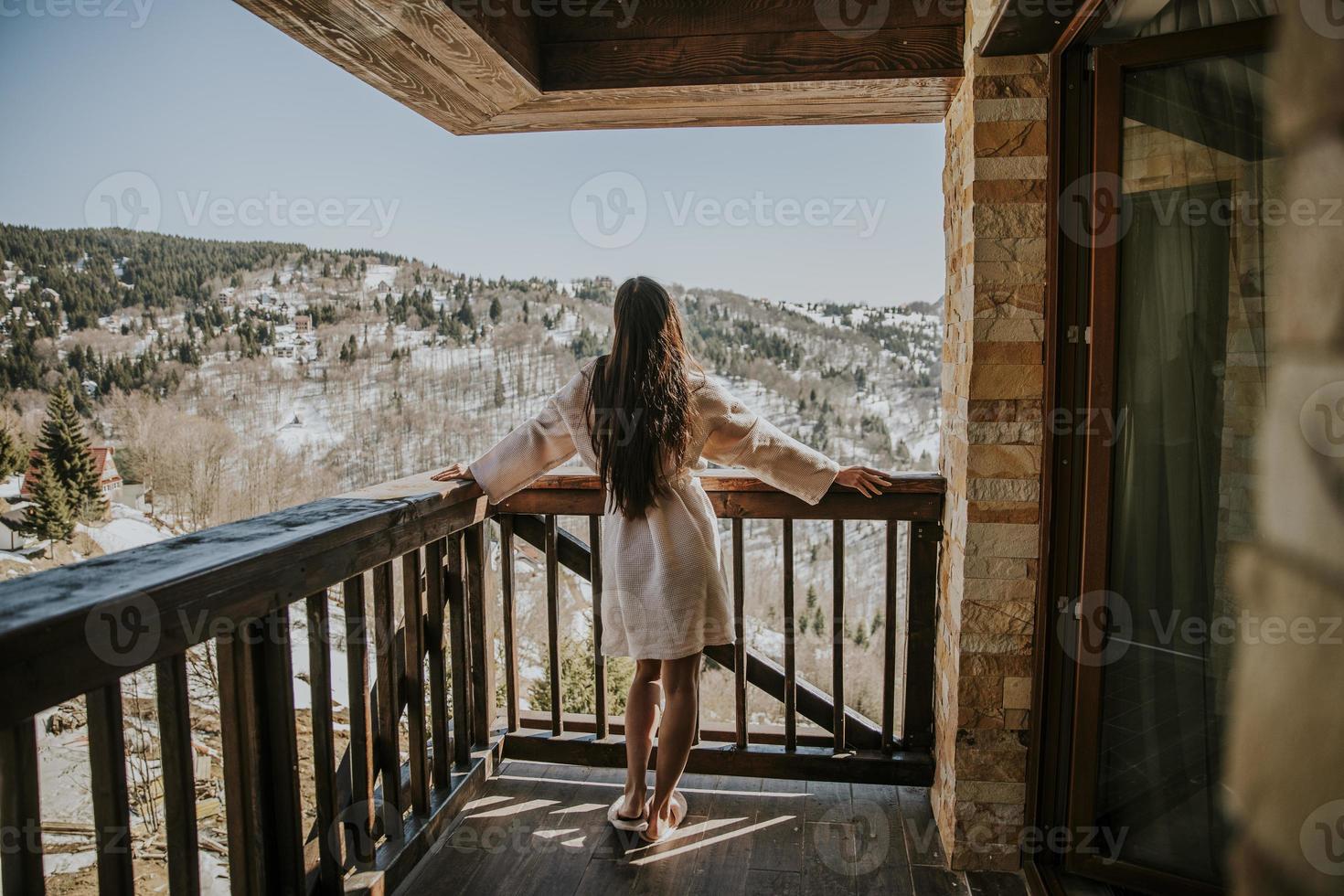 charmig ung kvinna i morgonrock som njuter av vinternaturen på den stora terrassen foto