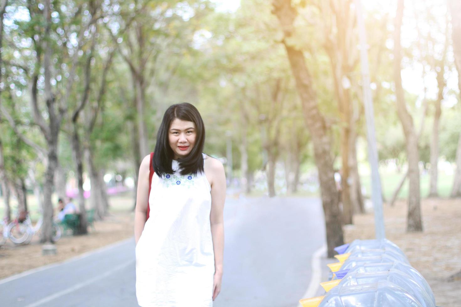 vacker asiatisk kvinna i vit klänning går och ler i naturparken. Thai flicka eller kinesisk flicka njuta på semester i trädgården foto