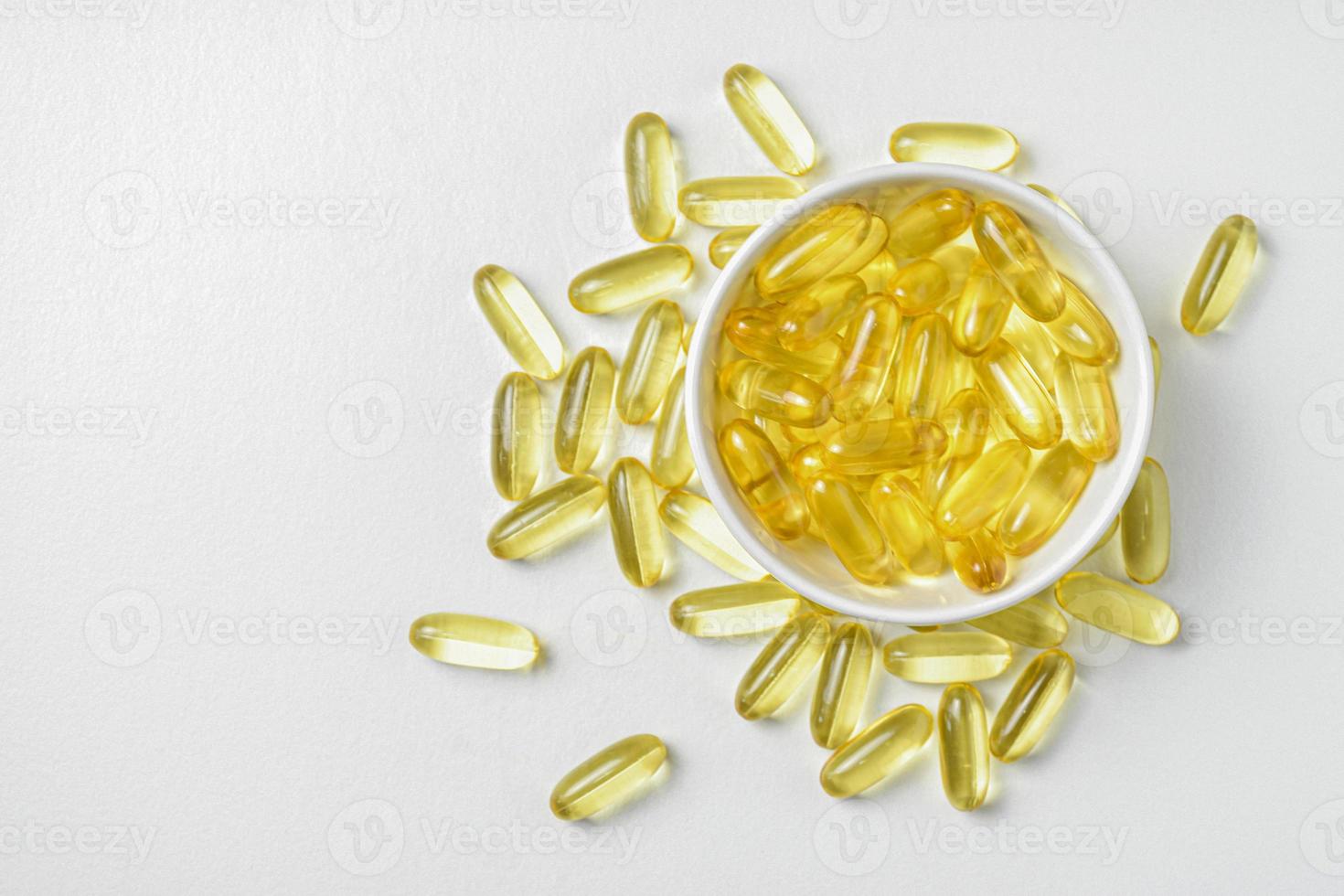 ovanifrån av guld fiskolja i skål isolerad på vit bakgrund. platt läggning av kompletterande föda. omega 3. vitamin e. kapslar laxfiskolja. kopiera sapce. foto