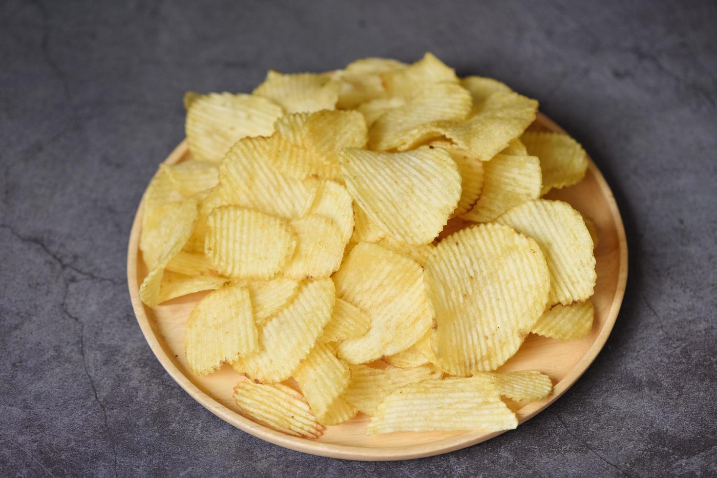 krispiga potatischips på köksbordet svart bakgrund, potatischips snack på tallriken - ovanifrån foto