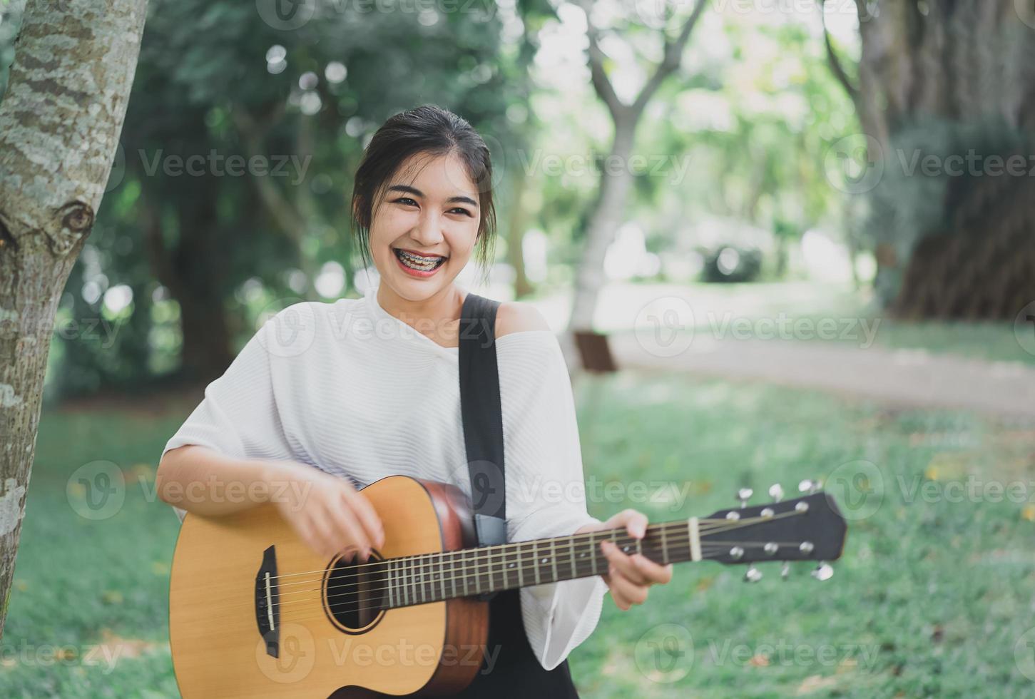 asiatisk ung kvinna spelar gitarr och sjunger musik i parken, asiatisk kvinna spelar gitarr i trädgården foto
