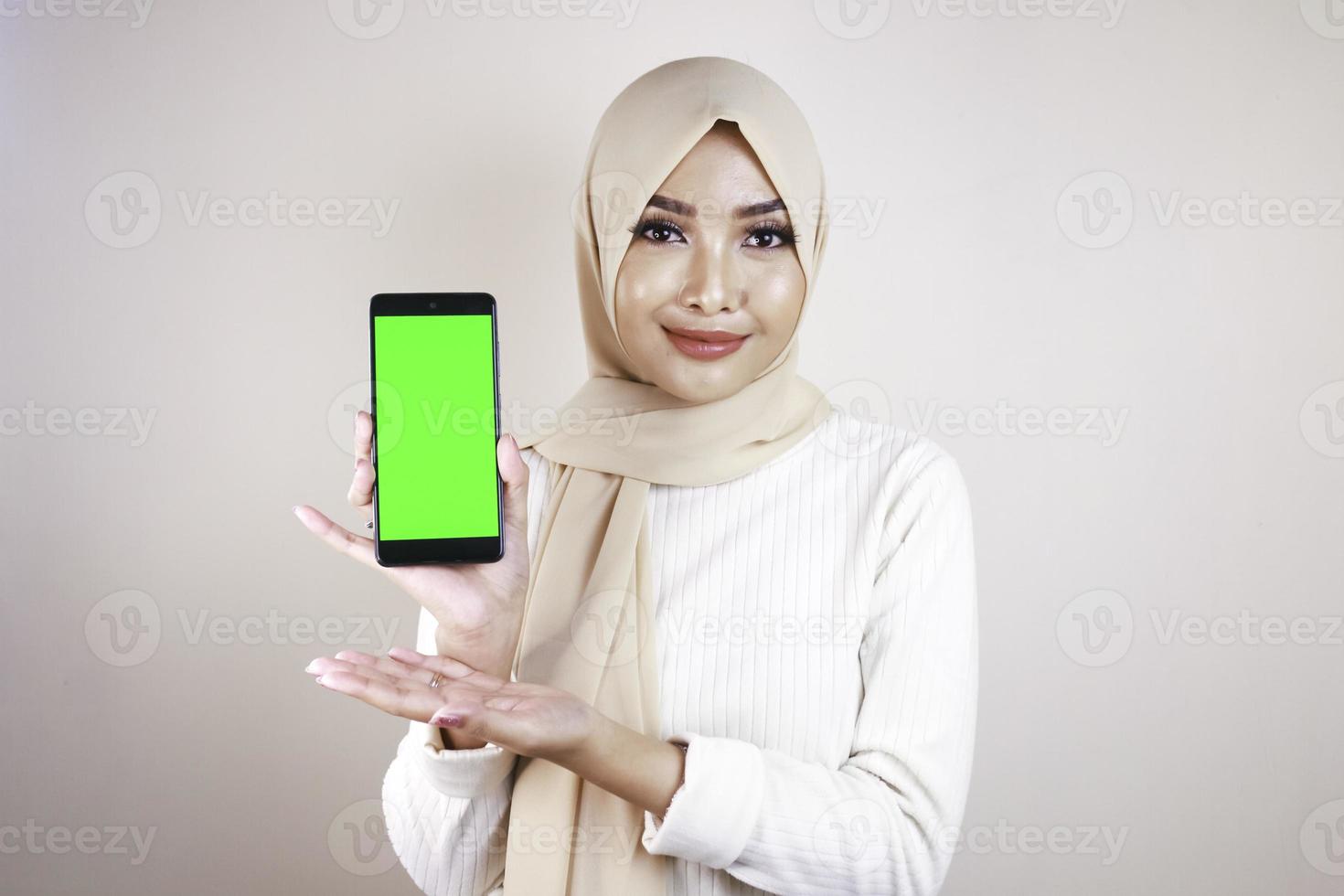 porträtt av glad ung muslimsk asiatisk kvinna som pekar på mobiltelefon med grön skärm foto
