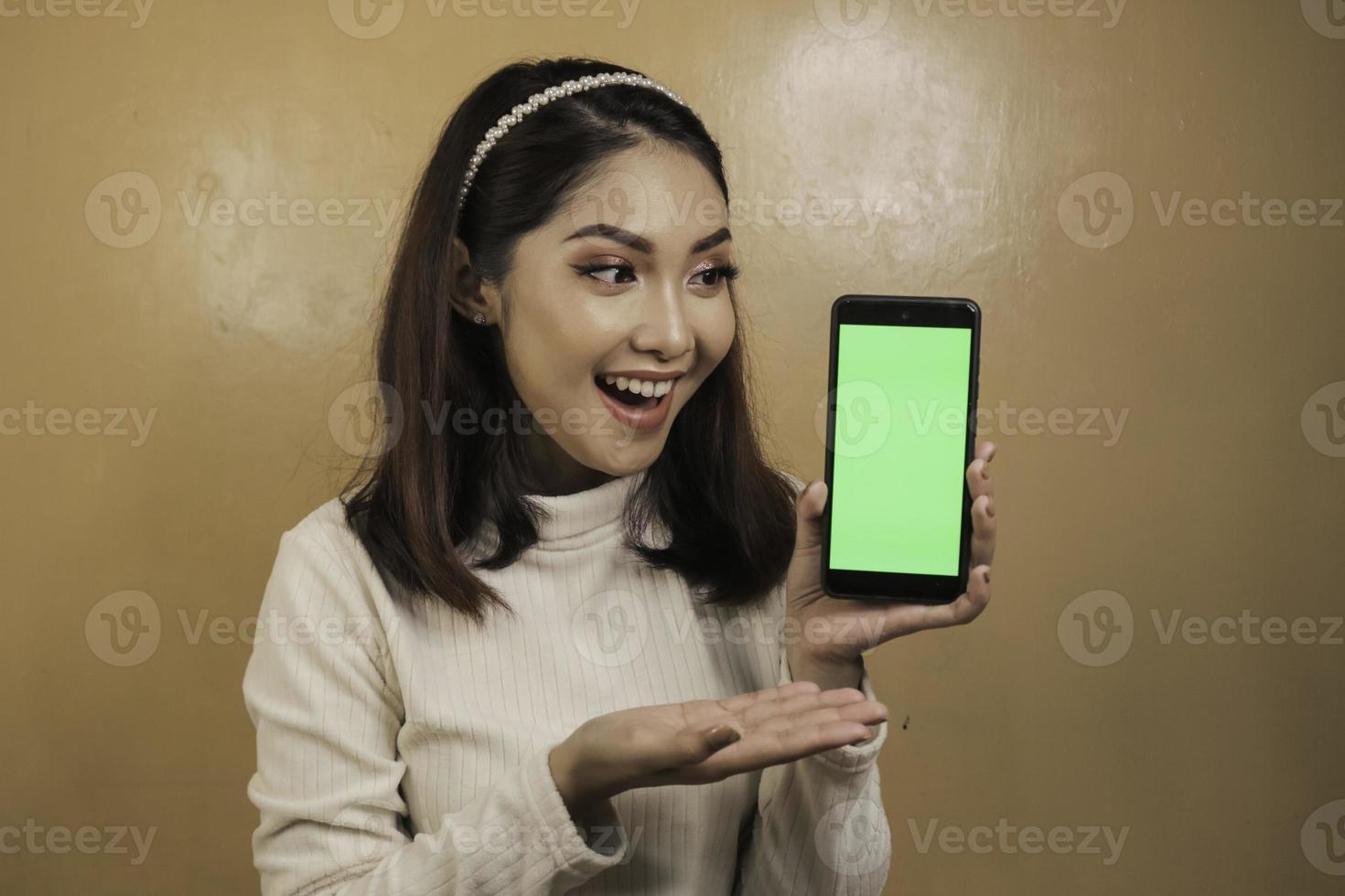 glada och leende unga asiatiska kvinnor som visar en grön tom skärm. foto