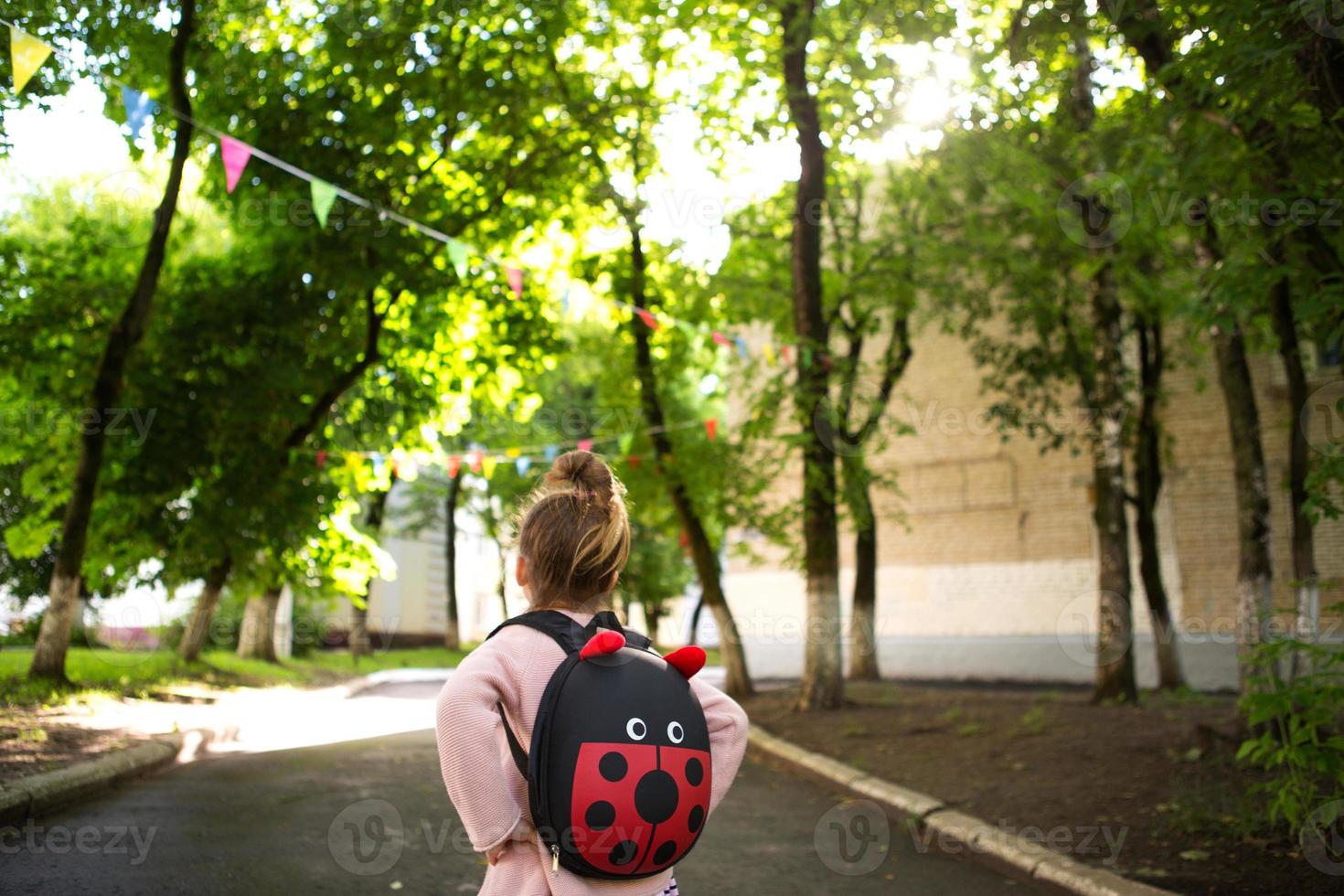 en liten flicka av kaukasiska i en skoluniform med en ryggsäck tittar på vägen på skolgården. koncept tillbaka till skolan. grundskola, utveckla verksamhet för förskolebarn. utrymme för text foto