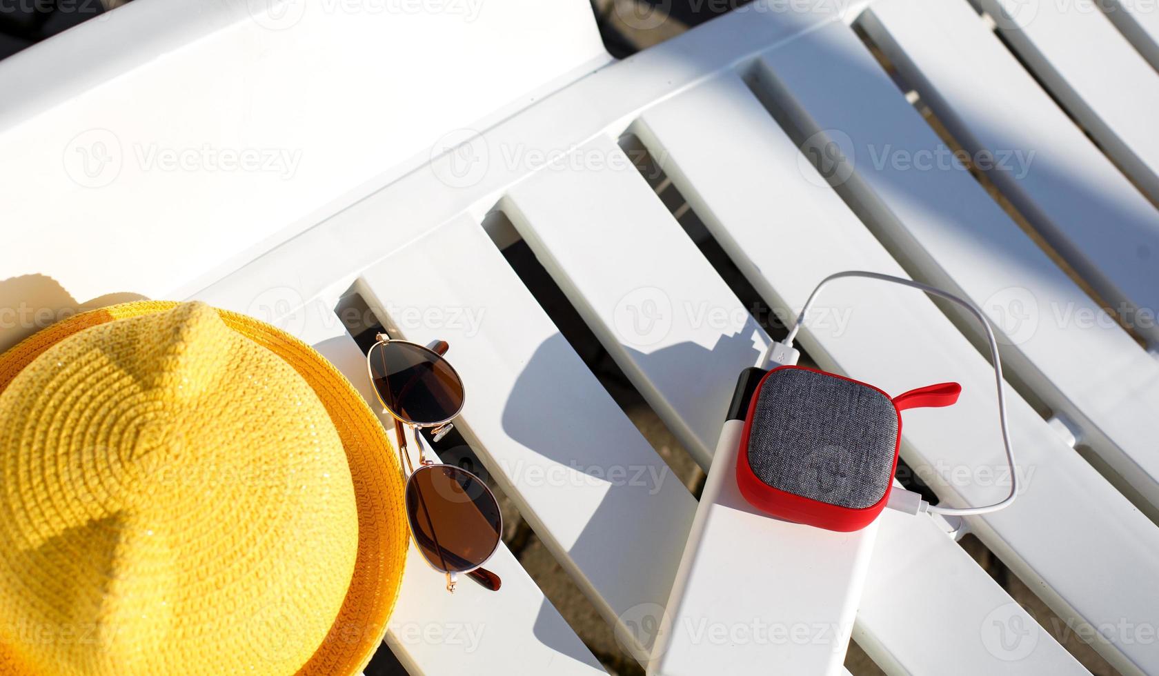 musik bärbar högtalare laddas från powerbanken via usb på en solstol nära poolen med strandtillbehör. alltid i kontakt, reseprylar, externt batteri för en smartphone. plats för text. foto