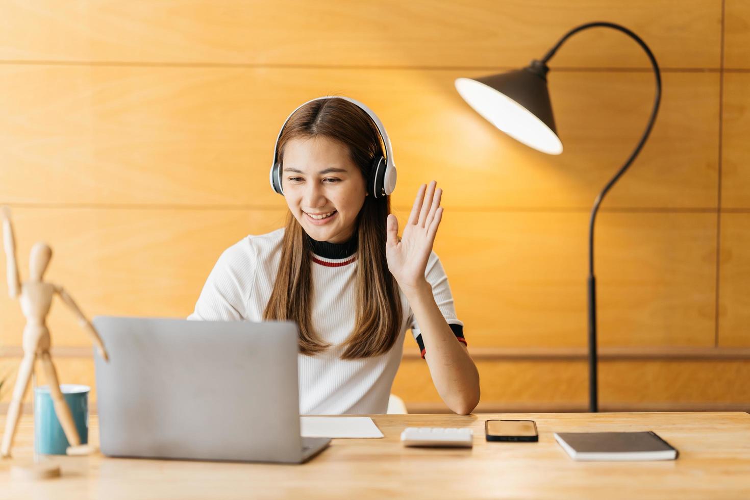 leende asiatisk ung kvinna som använder headset tittar på laptop skärm lyssna och lära sig onlinekurser. glad kinesisk affärskvinna med hörlurar videosamtal för kundtjänst foto