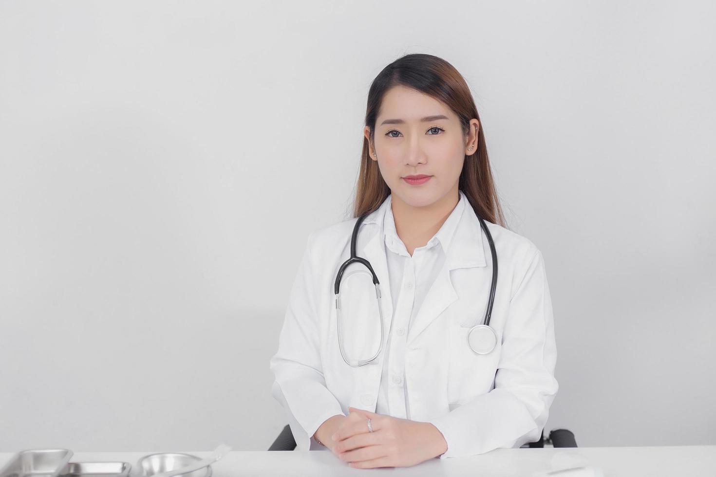 asiatisk kvinnlig läkare tittar rakt på sjukhuset bär en vit rock och ett stetoskop på en vit bakgrund hälso-och sjukvård koncept. foto