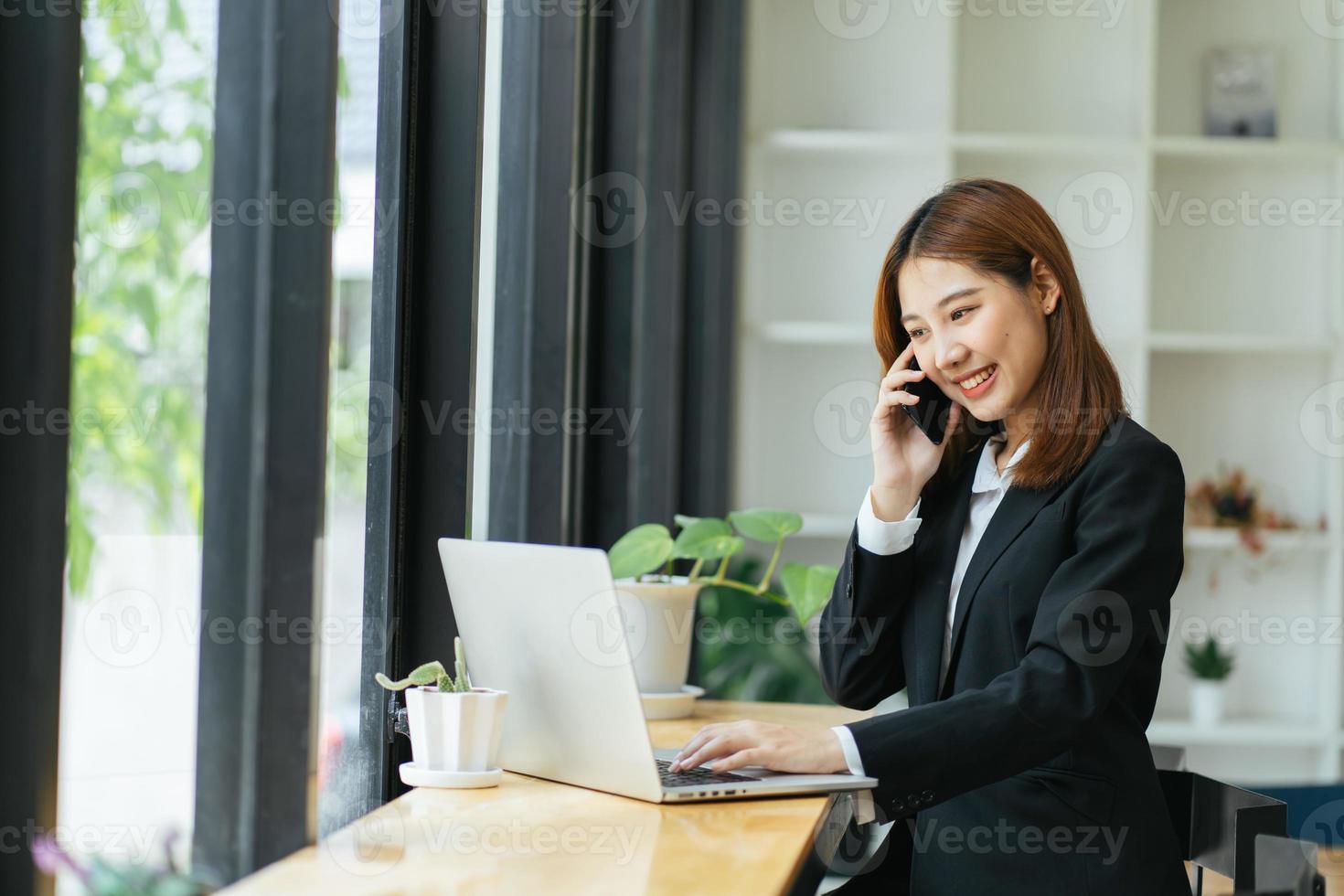 asiatisk affärskvinna i formell kostym på kontoret glad och glad när du använder smartphone och arbetar foto