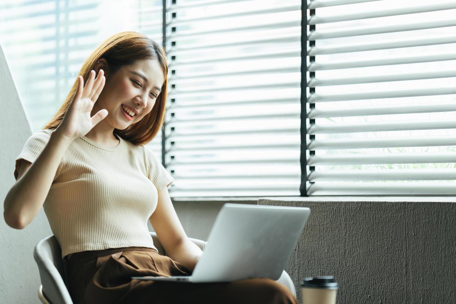 asiatisk kvinna med videosamtal på sin dator hemma. leende flicka studerar online med lärare. foto