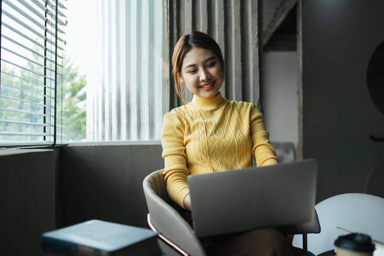 porträtt av vacker asiatisk kvinna som sitter inomhus på kaférestaurang under sommaren, med hjälp av smart trådlös teknologi dator bärbar dator och smartphone, avkopplande kaffepaus på kaférestaurang. foto