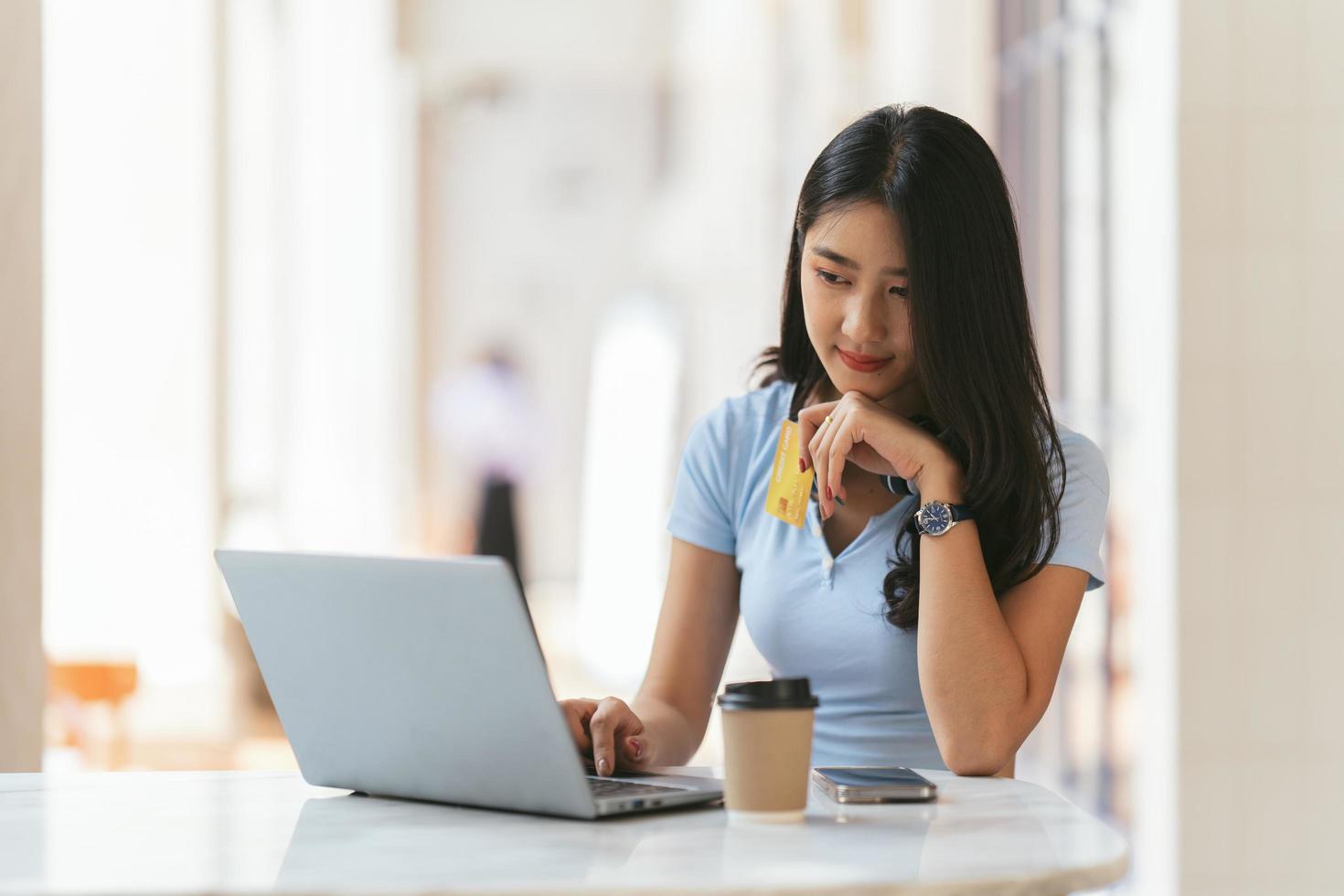 online bankkoncept. porträtt av glad ung asiatisk kvinna med bärbar dator och kreditkort sitter på café, leende asiatiska kvinnor njuter av att göra betalningar hemifrån. foto