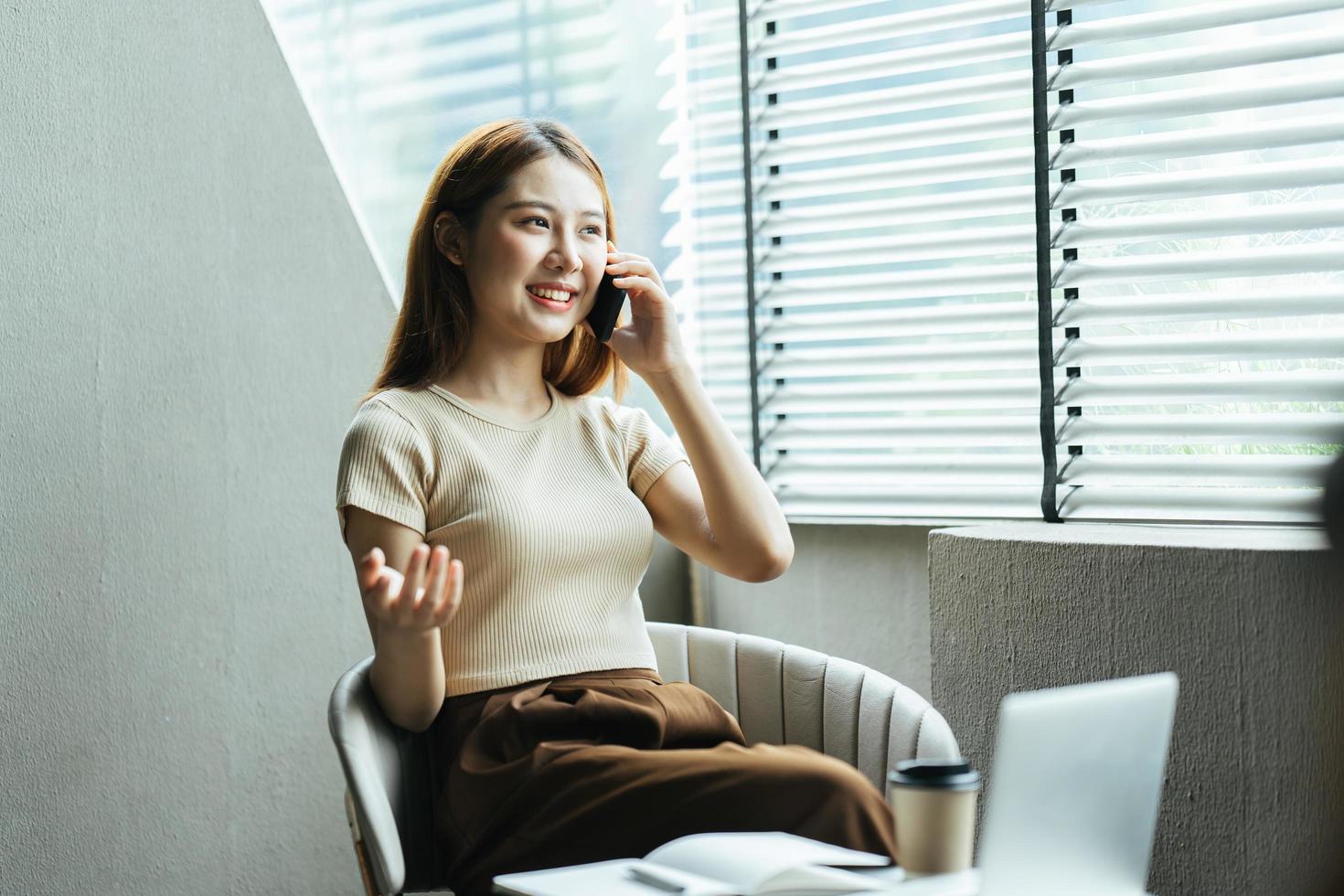 asiatisk kvinna i vardagskläder är glad och glad medan hon kommunicerar med sin smartphone och arbetar på ett kafé. foto