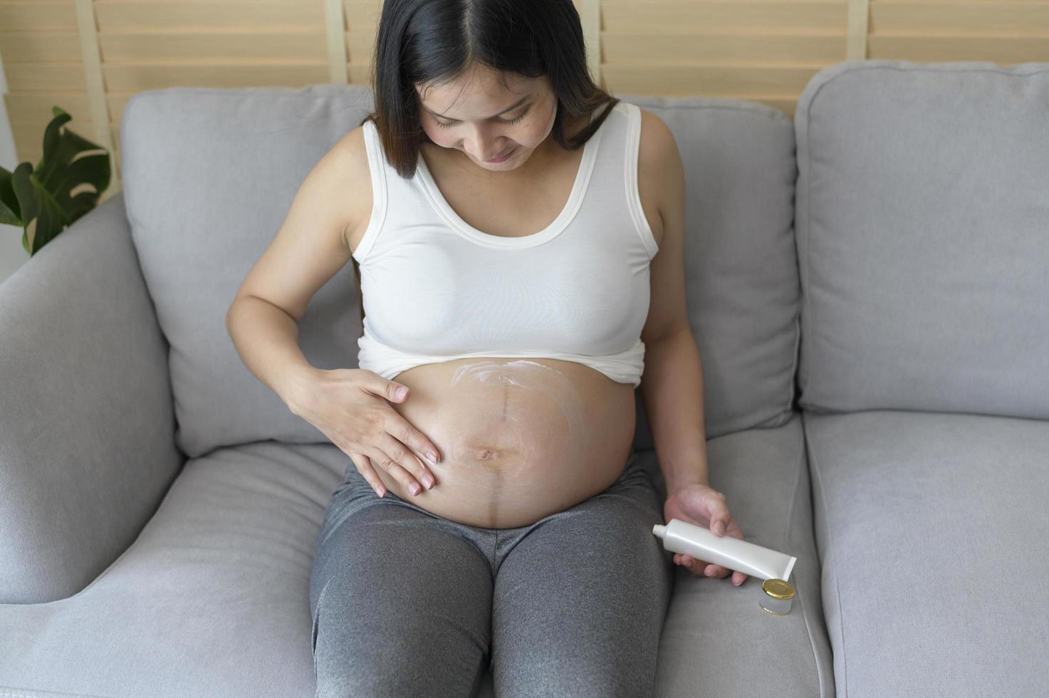 ung gravid kvinna applicerar fuktgivande kräm på mage, sjukvård och graviditetsvård foto