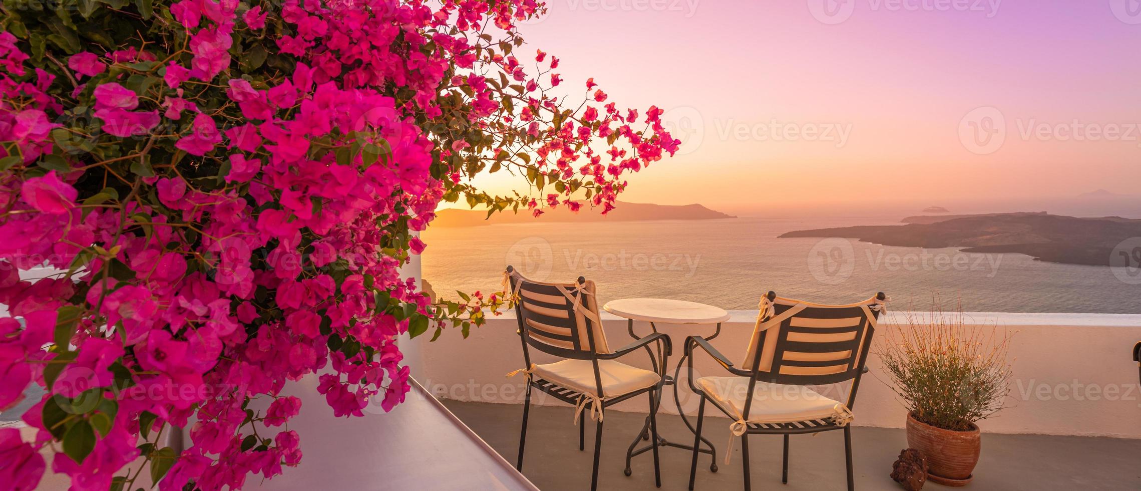 vacker utsikt över kalderan och njuta av romantiska landskap solnedgången Egeiska havet, santorini. par resor semester, smekmånad destination. romantik med blommor, två stolar bord och havsutsikt. lyxsemester foto