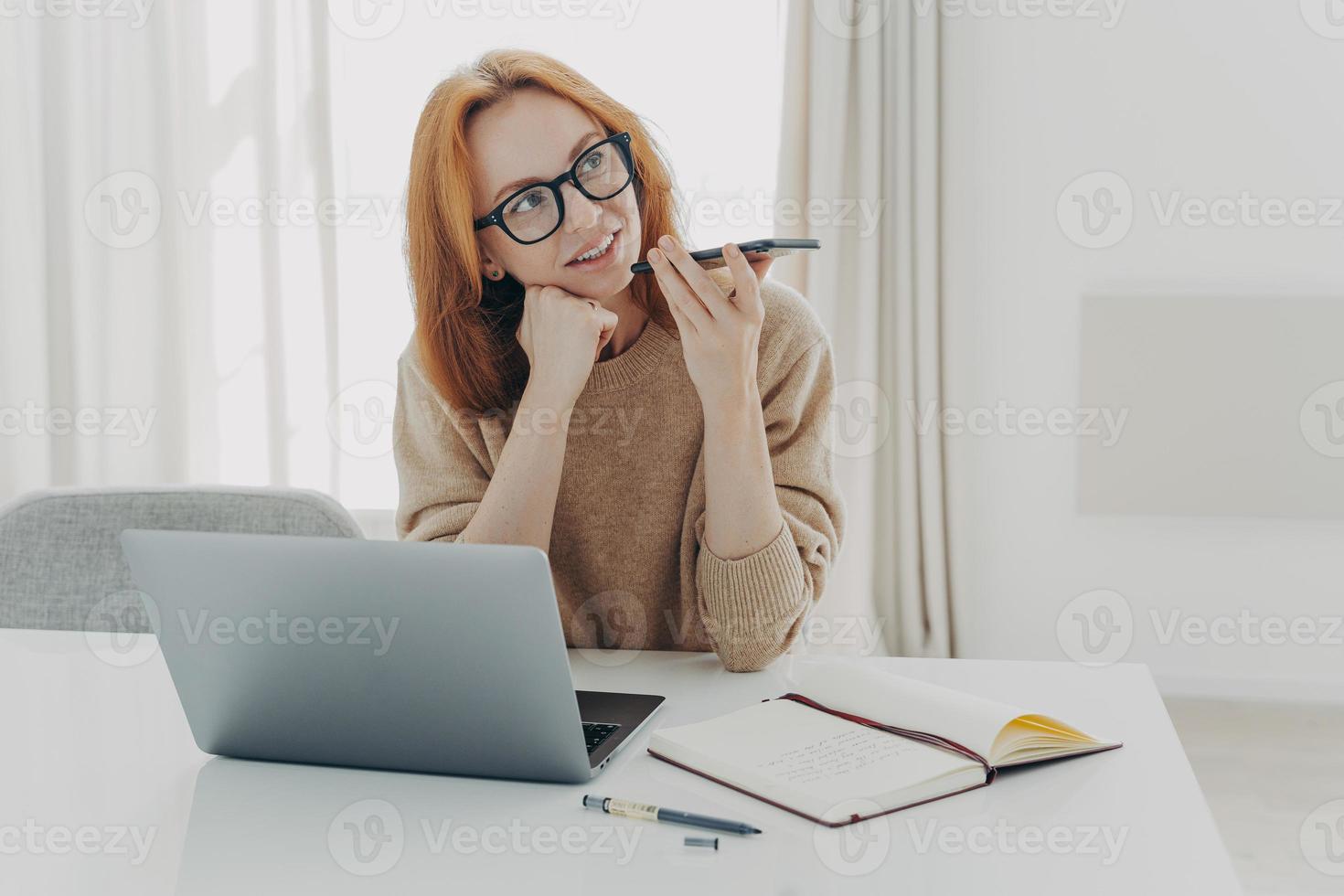 kvinnlig frilansare spelar in röstmeddelande sitter vid skrivbordet gör anteckningar i anteckningsblock foto