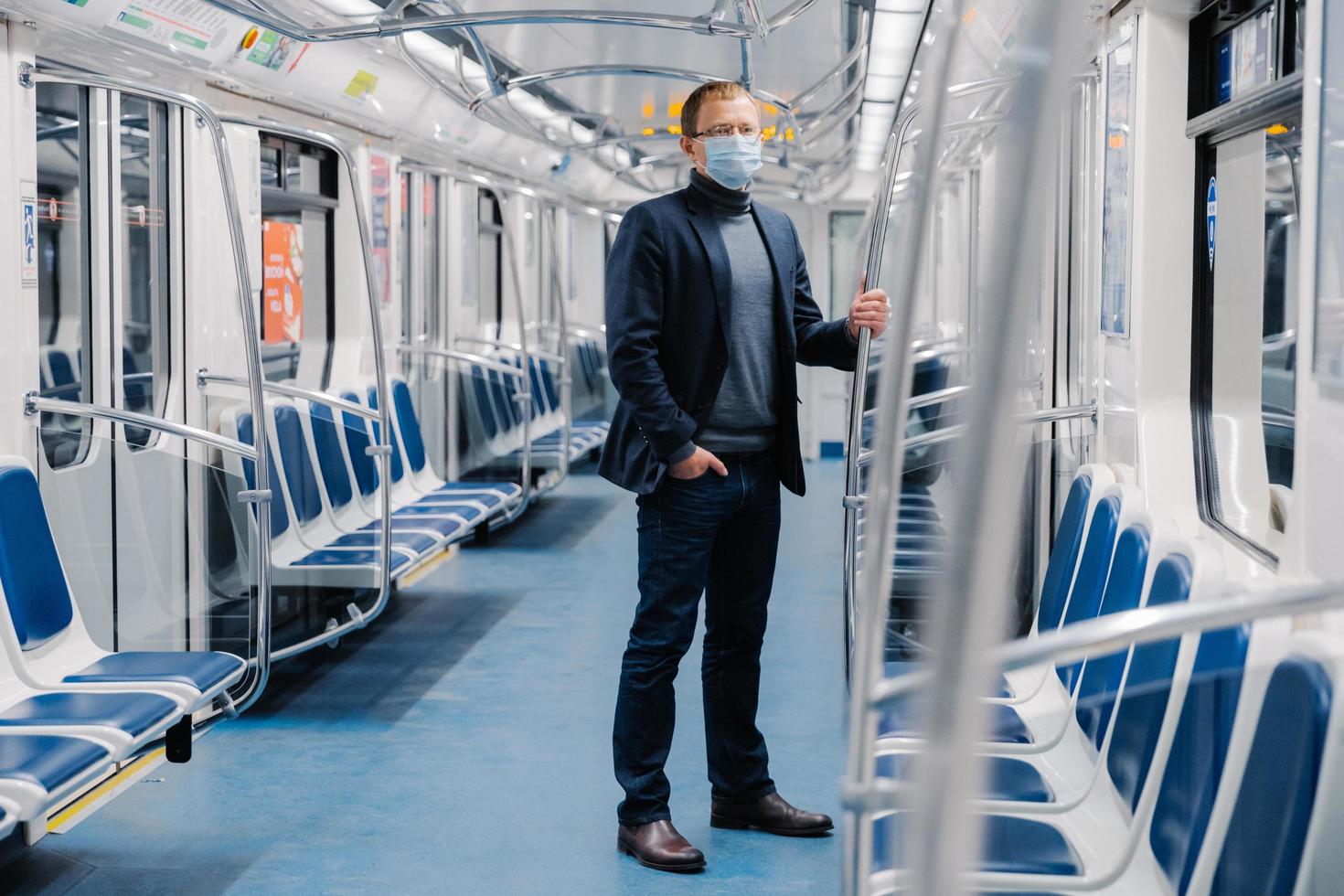 fullängdsbild av manlig entreprenör i formell kostym, medicinsk mask, står i stadståg under sjukdomsutbrott, virusskydd och karantän skyddar sig mot coronavirus i kollektivtrafiken foto