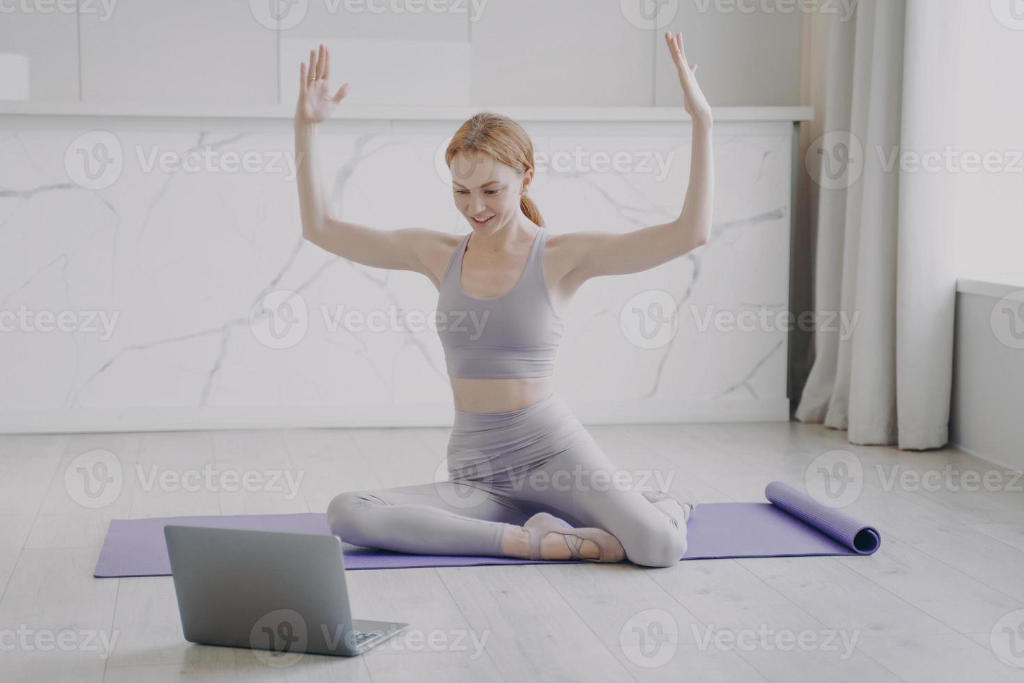 smal sportig tjej som sträcker sig på mattan. online fjärrträningskurser student tittar på video på bärbar dator. foto