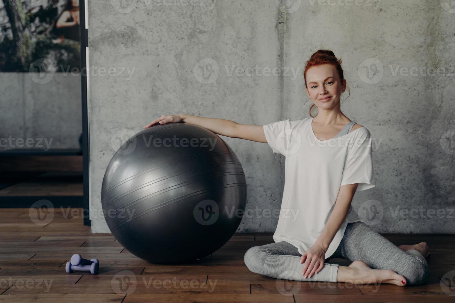 glad ung fitness kvinna koppla av efter pilates träning när du sitter med stor träningsboll på golvet foto