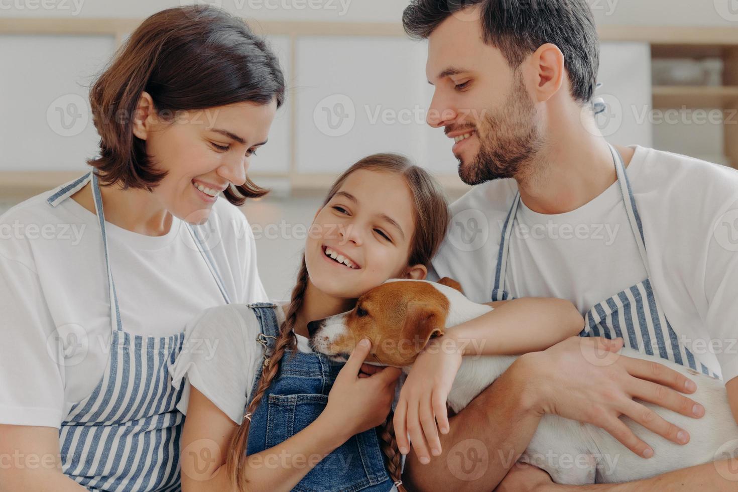 glad härlig familj leende och uttrycka uppriktiga känslor, njut av att umgås i mysiga hem. leende litet barn glad förälder köpte hennes nya husdjur, mysa jack russell terrier med kärlek och omsorg. foto