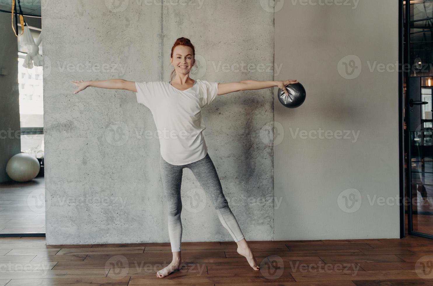 smal vacker rödhårig kvinna som utför barre övningar i fitnessstudio foto