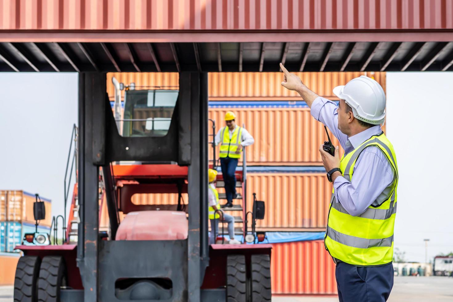 ung manlig ingenjör eller chef användning av radiokommunikation för att kontrollera containerlast i industri framför maskinlyftcontainer och lastutrymme. transport- och logistikkoncept. foto