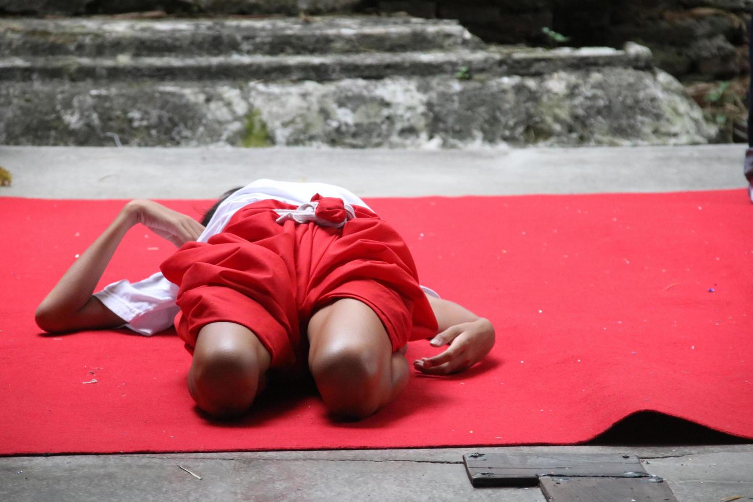 ett barn övar sin kropp på röda mattan vid cementgolvet för att lära sig khon, bangkok. khon är en dansdramagenre i thailand. foto