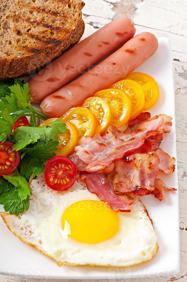 engelsk frukost - stekt ägg, bacon, korv och rostat rågbröd foto
