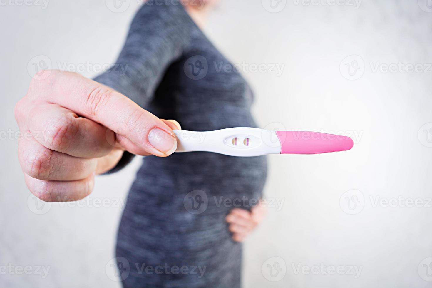 ung gravid kvinna med svullen mage håller ett graviditetstest foto