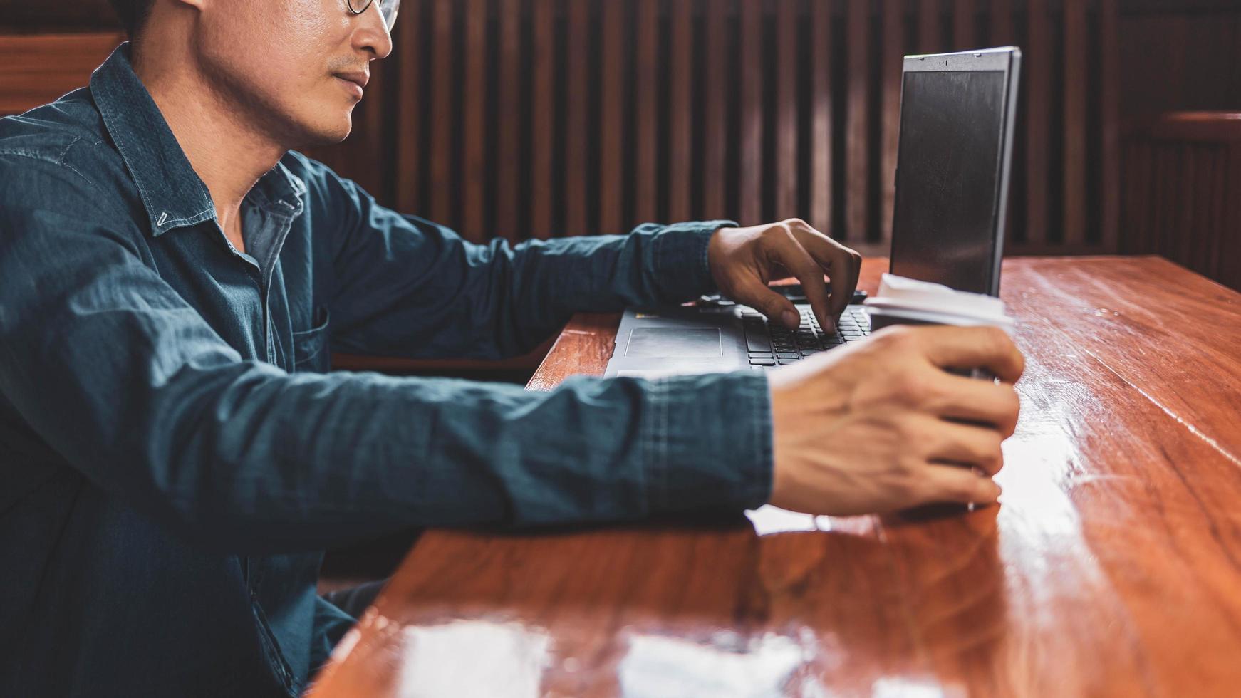 en ung man med glasögon som använder en bärbar dator som skriver på ett tangentbord, skriver e-postmeddelanden eller arbetar online på en dator i sitt vardagsrum. foto