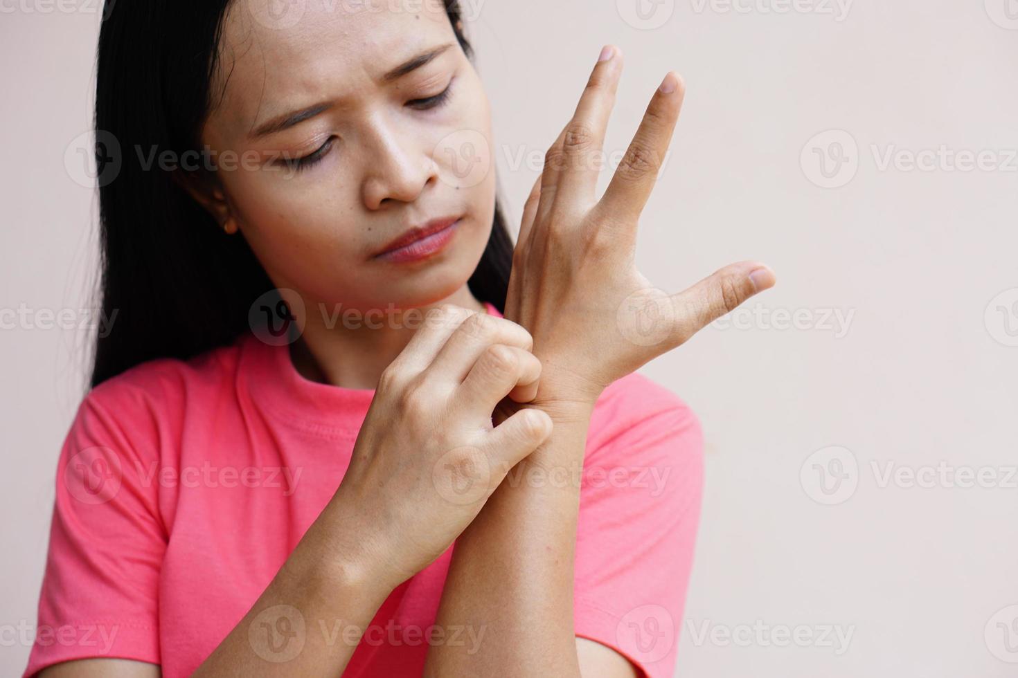 kvinna kliar arm från klåda på ljusgrå bakgrund. orsaken till kliande hud inkluderar insektsbett koncept av sjukvård hud. foto