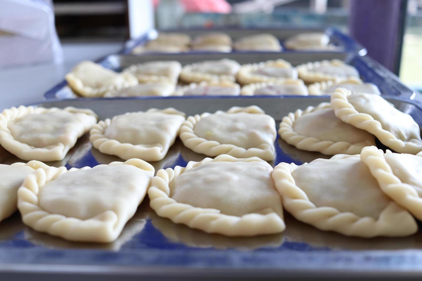 råa currypuffar ligger på rostfria brickor innan de steks i olja, thailand. foto