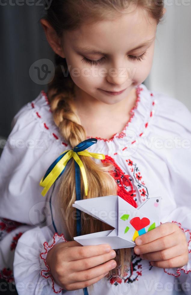 en liten ukrainsk flicka i traditionella kläder håller en pappersduva av fred i sina händer foto