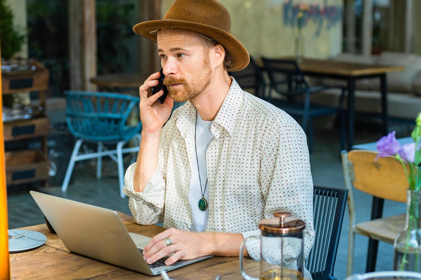 ung snygg hipster i hattarbete med bärbar dator utomhus på gatukaféet foto
