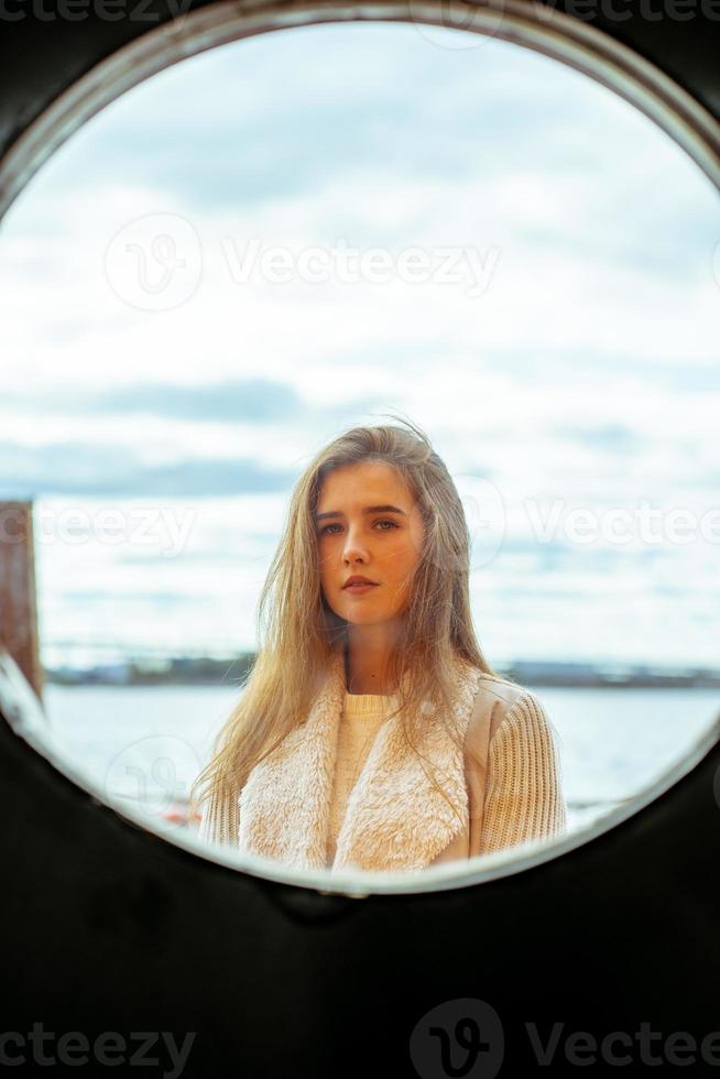 ansiktet av ung flicka i rund ram fönster på bakgrund av havet, havet, vid vattnet. porträtt i cirkel, bakgrundsbelyst, vertikal foto