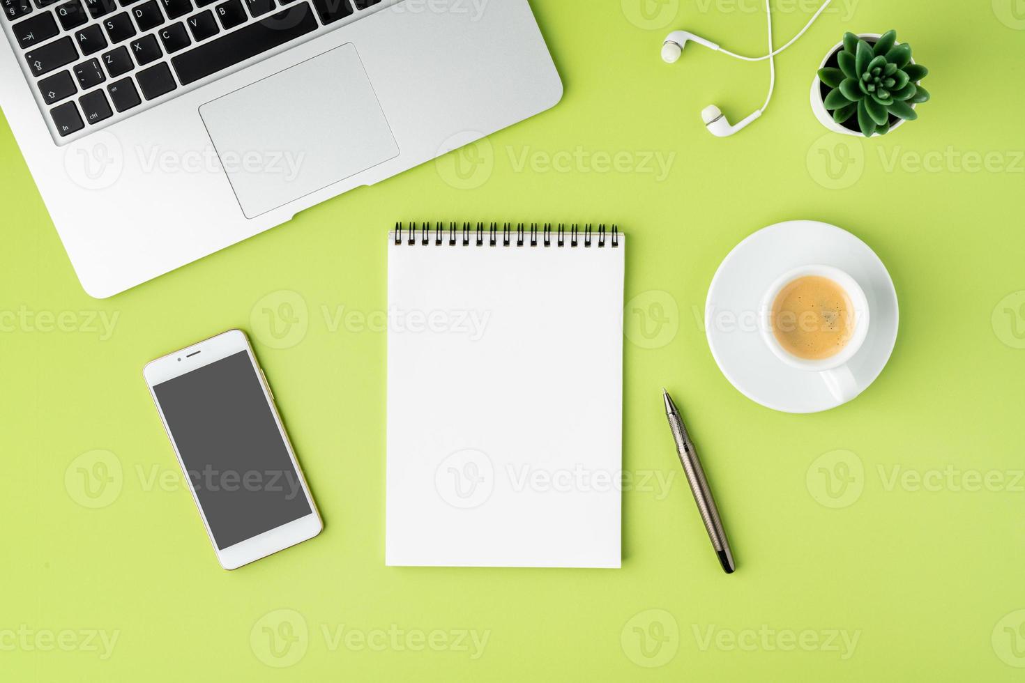 begreppet modern arbetsyta. anteckningsbok, smartphone, kaffekopp, bärbar dator och hörlurar på grön bakgrund foto