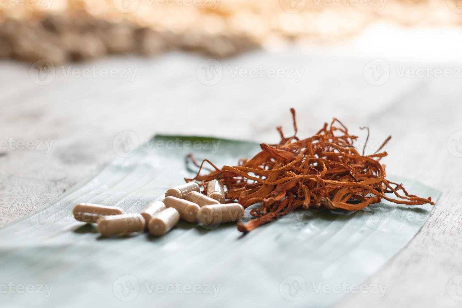 torr cordyceps militaris på ett grönt bananblad med träbakgrund. orange medicinsk svamp för god hälsa med kapslar. foto