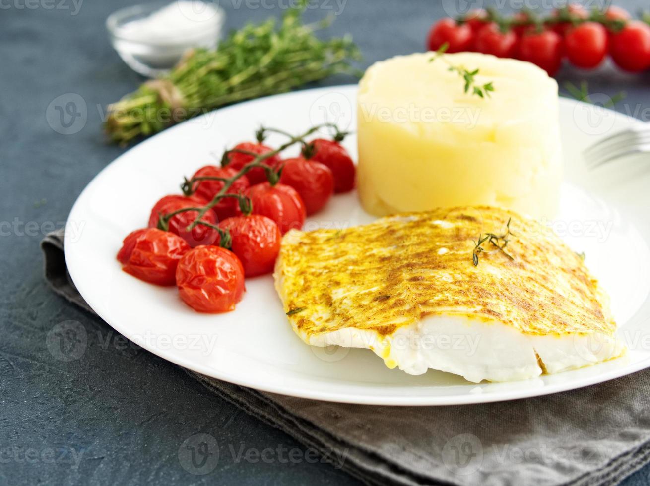 fisk torsk bakad i ugn med potatismos, tomater, diet hälsosam mat. mörkgrå bakgrund foto