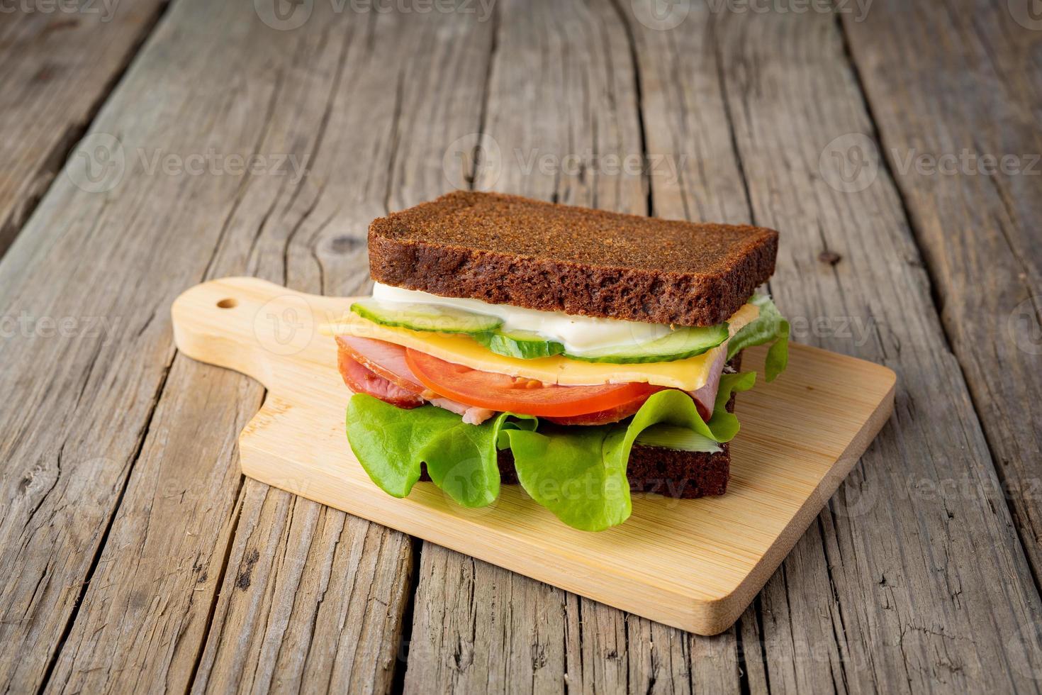 smörgås med svart rågbröd, skinka, ost, tomater, gurkor, sallad på mörk träbakgrund foto