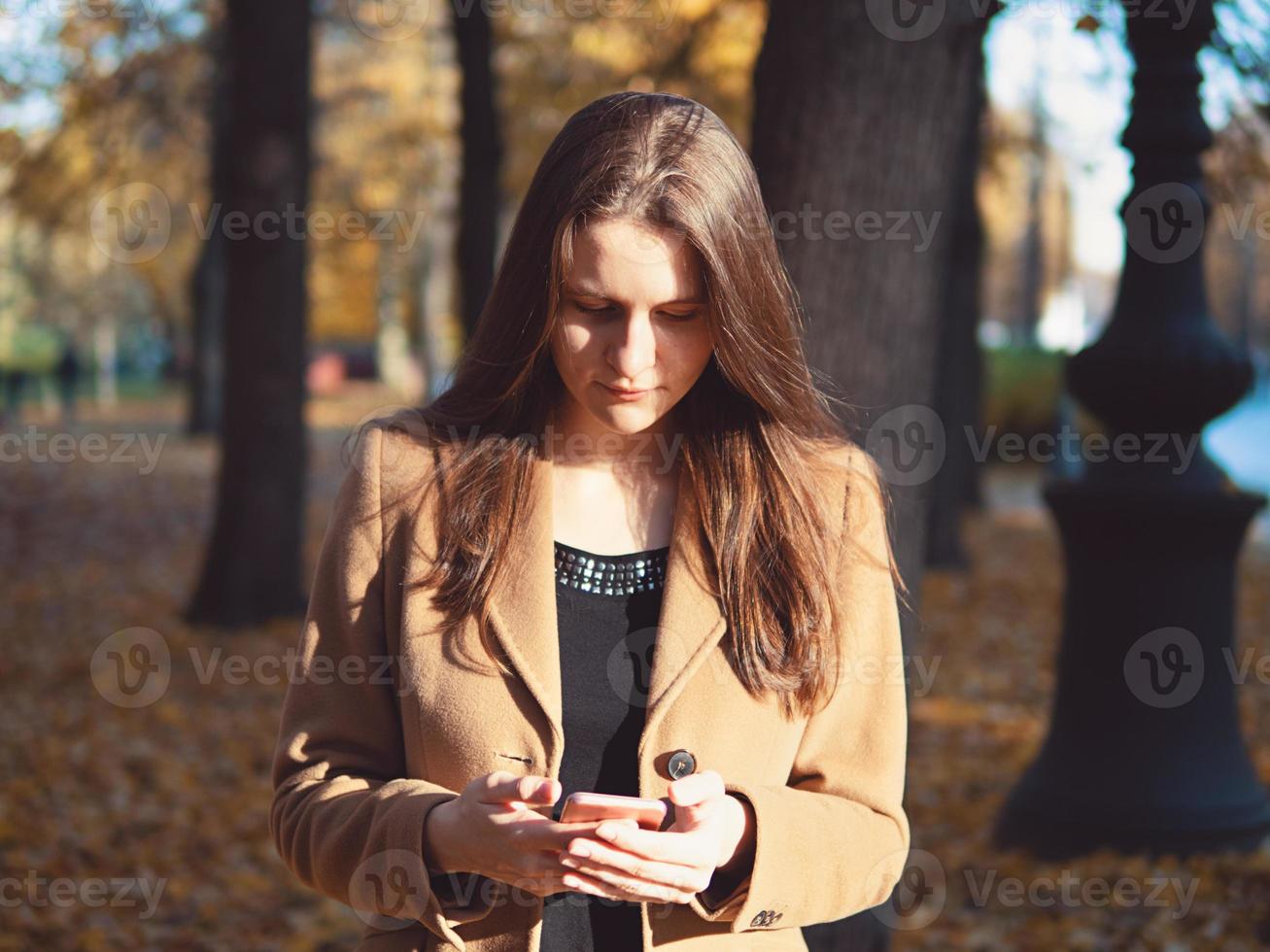 vacker tonårsflicka i parken, håller smartphone och chattar online på internet. ung kvinna med långt hår foto