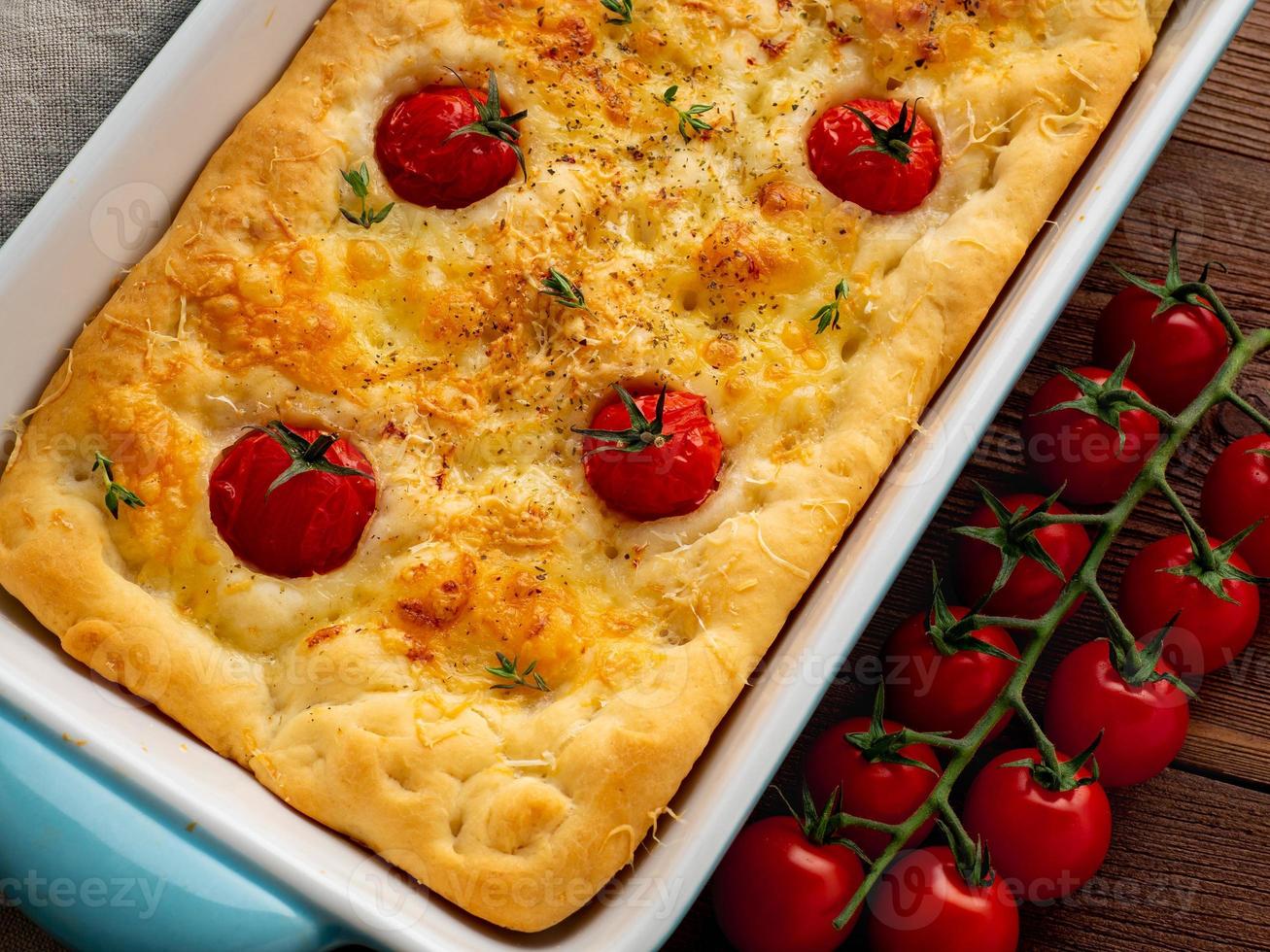 aptitretande gyllene focaccia med tomater och kryddor, på mörkt rustikt träbord foto