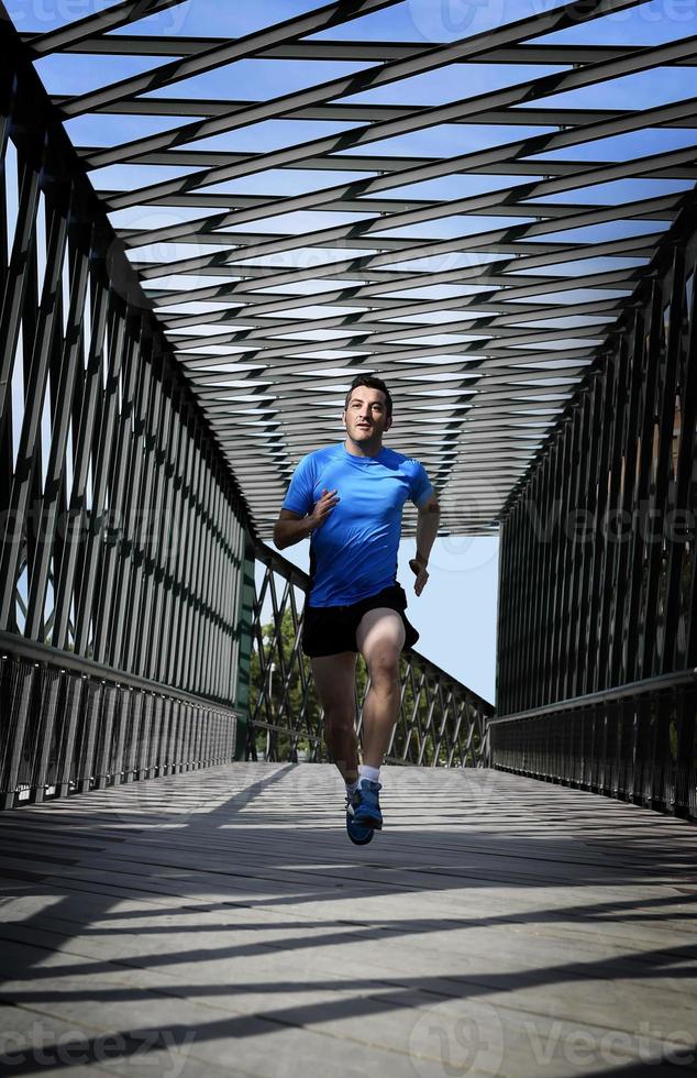ung atletisk man som utövar löpning som passerar urban city bridge foto