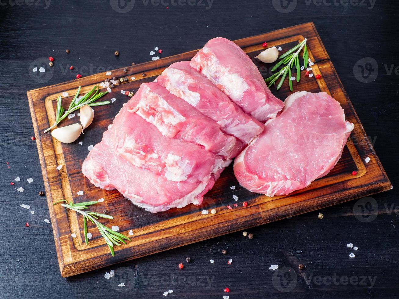 fläskbiff, rå karbonatfilé på mörk bakgrund, kött med rosmarin, kryddor, sidovy foto