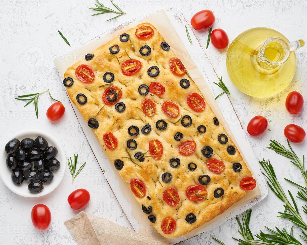 focaccia med tomater, oliver och rosmarin, ovanifrån. hela italienska plattbröd, flaska med olja foto