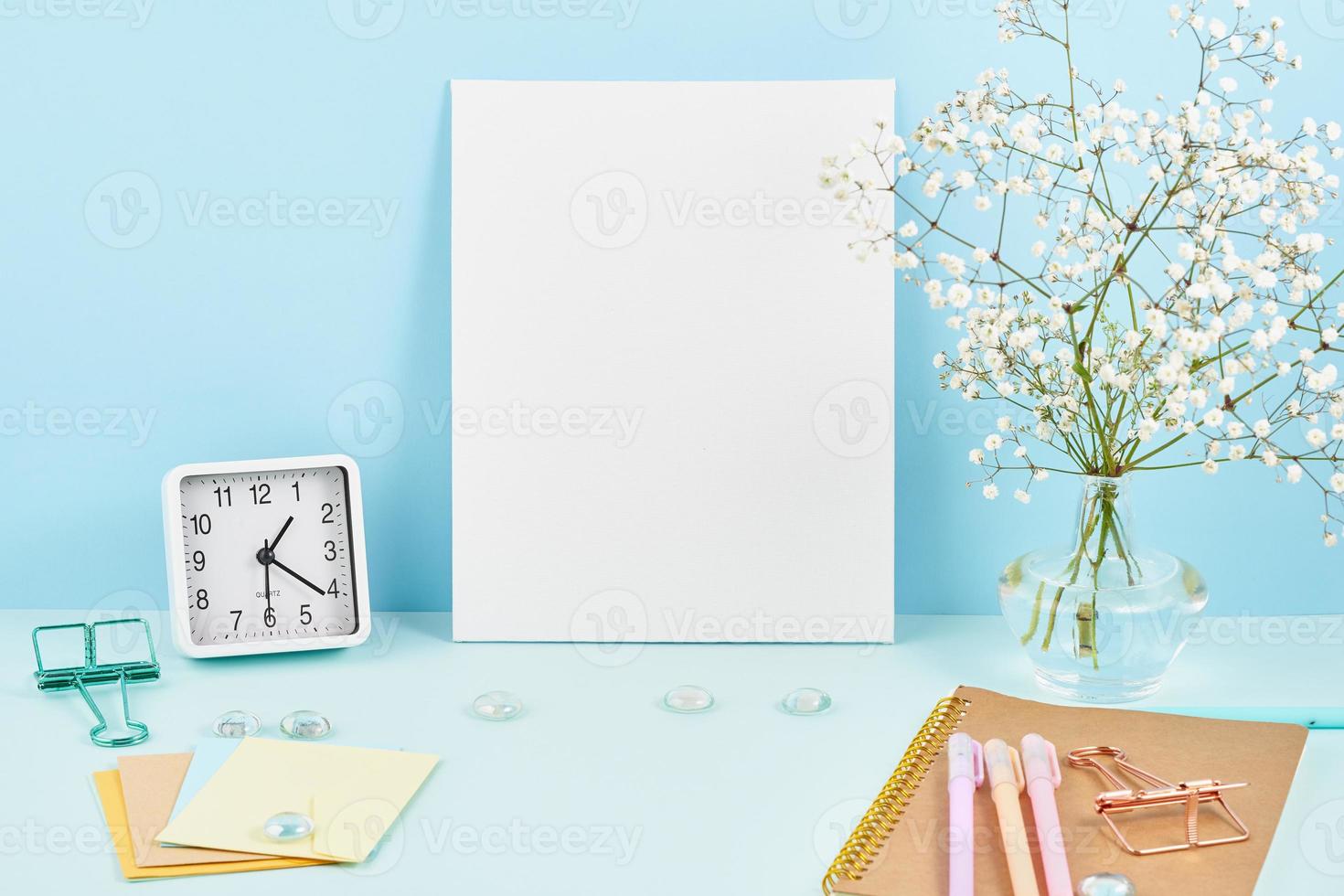 mockup med tom vit ram på blått bord mot blå vägg, larm, blomma i vaze. foto