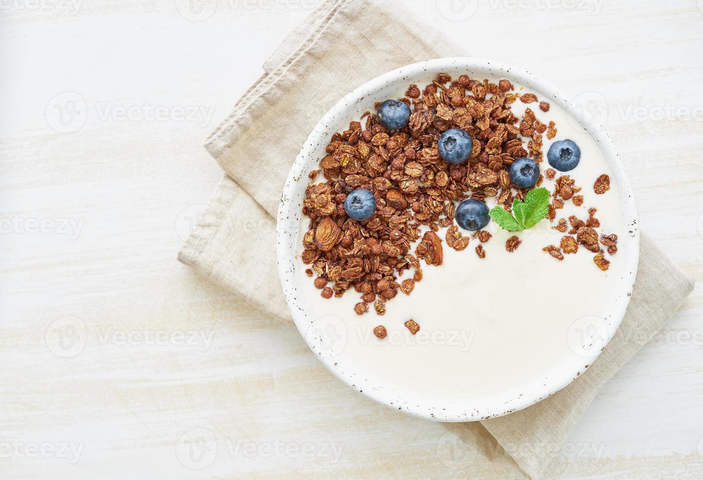 yoghurt med chokladgranola, blåbär. frukost på en vit rustik bakgrund, ovanifrån foto