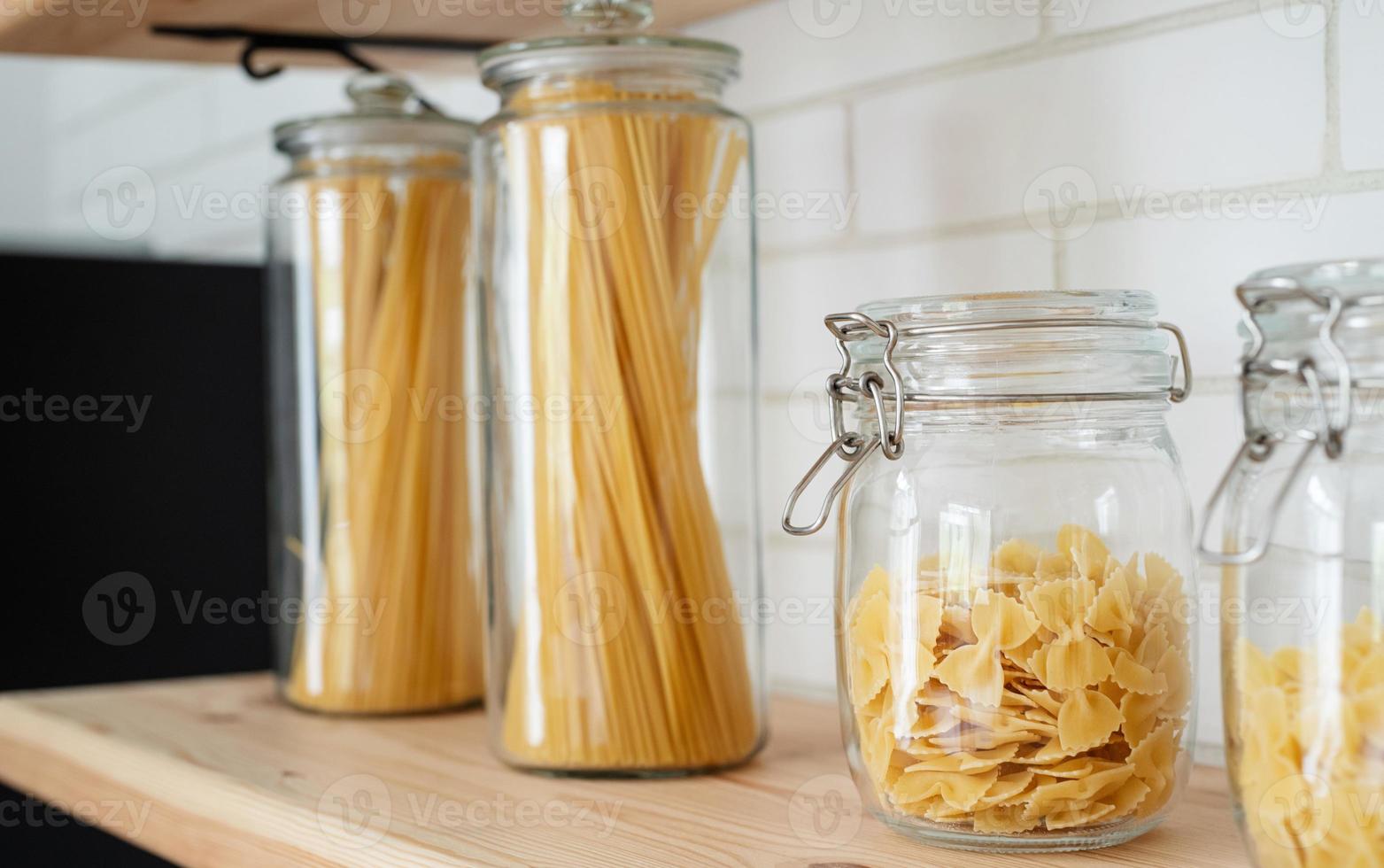 vete italiensk pasta i glasburk på en trähylla i köket. foto