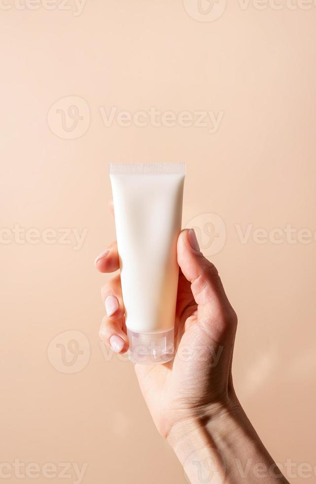 ansiktskräm mock-up. kvinnlig hand som håller vit grädde tub på beige bakgrund foto